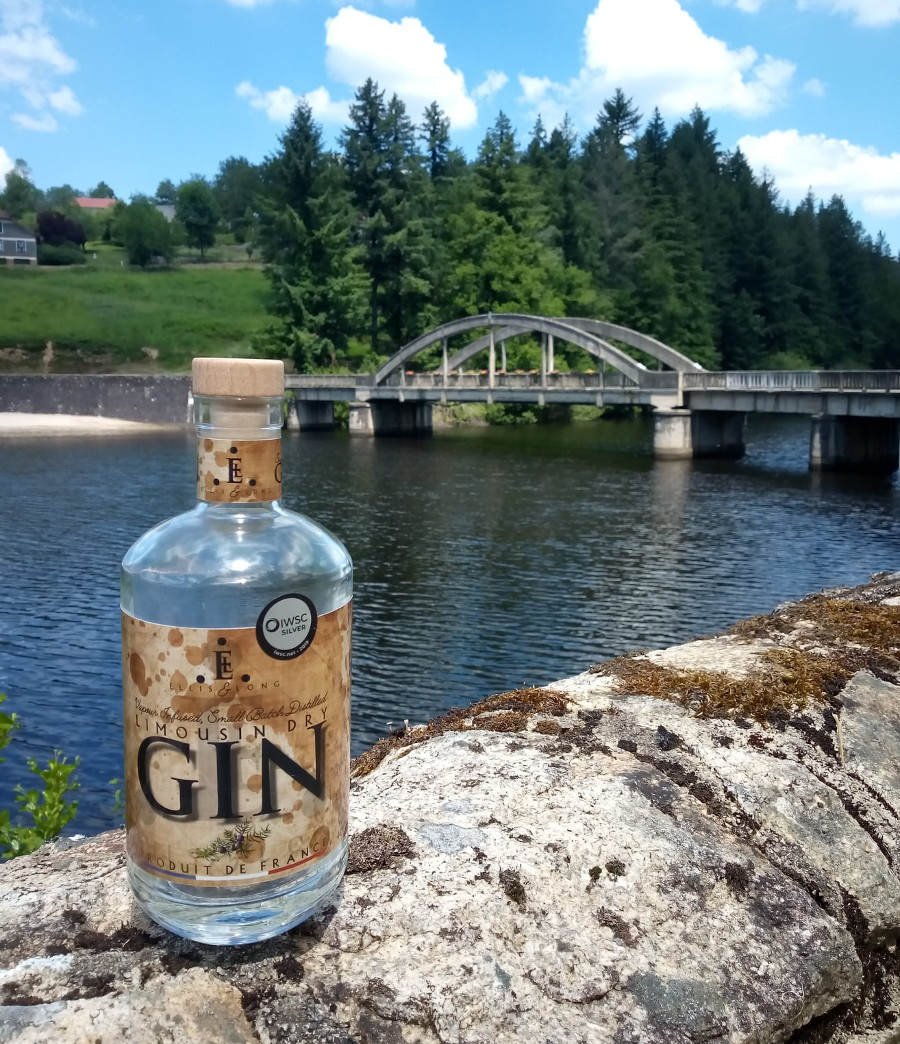 A bottle of Limousin Dry Gin placed on a stone wall in Chatelus-le-Marcheix overlooking the Taurion river with the bridge in the background.